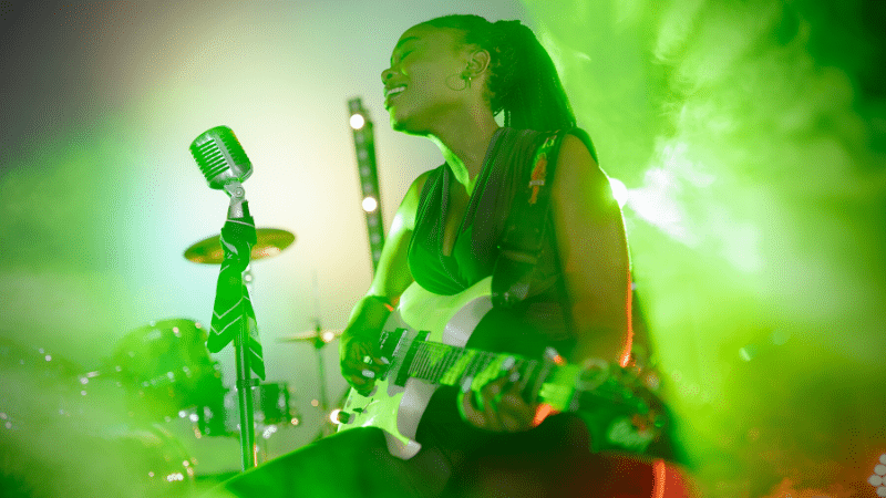 A woman singer playing a guitar in front of green smoke.