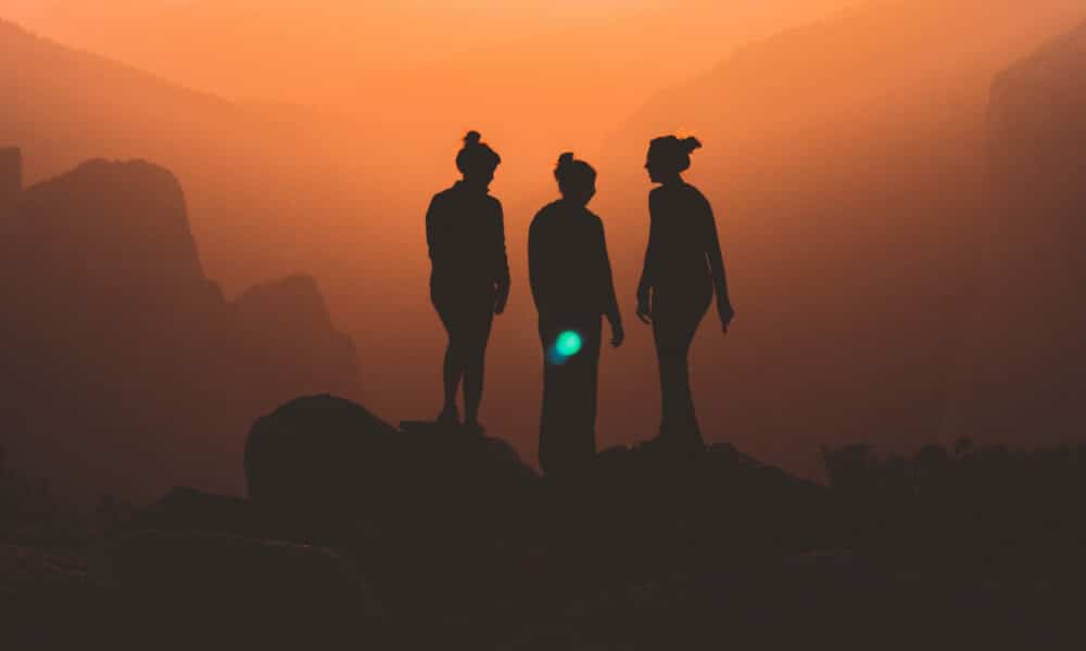 Three empowered women standing on top of a mountain at sunset.