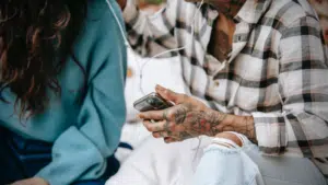 A man and woman enjoying playlist music on a cell phone.