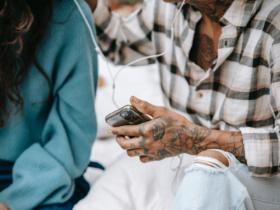 A man and woman enjoying playlist music on a cell phone.