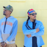 Two men posing in front of a vibrant yellow wall.