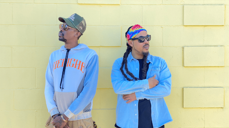 Two men posing in front of a vibrant yellow wall.