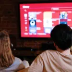 Two people in sync watching tv in front of a red tv.