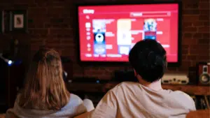 Two people in sync watching tv in front of a red tv.