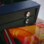 A vinyl record player sits on a table next to a stack of records.