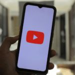 A person holding up a phone featuring the YouTube Shorts logo.