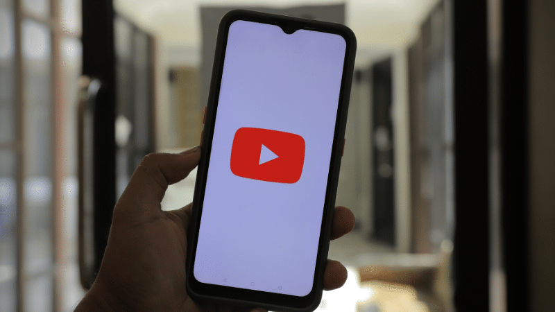 A person holding up a phone featuring the YouTube Shorts logo.