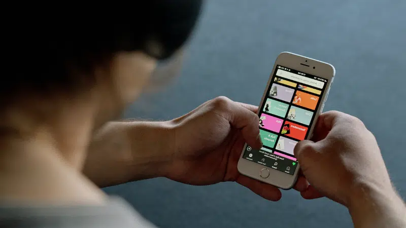 A person holding a cell phone with a Spotify app.