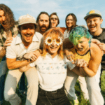 A diverse group of people posing for a picture in a field, representing the LGBTQIA+ community.