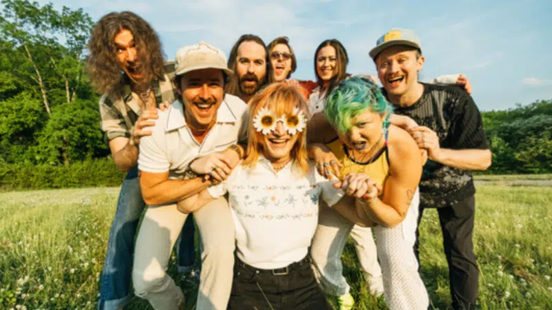 A diverse group of people posing for a picture in a field, representing the LGBTQIA+ community.