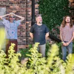 A group of men performing fresh new music in front of a brick building.