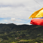 A yellow, blue, and red flag waves against a backdrop of green hills and a cloudy sky, like a banner heralding a grand conference in unity’s colors.