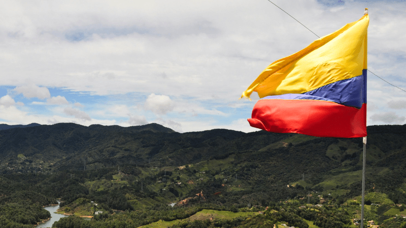 A yellow, blue, and red flag waves against a backdrop of green hills and a cloudy sky, like a banner heralding a grand conference in unity’s colors.