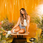 A fresh woman sitting on a table surrounded by flowers.