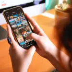 A woman using Instagram on her smartphone while sitting in front of a computer.