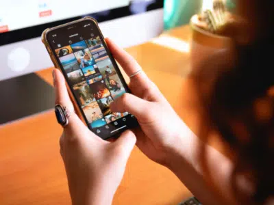 A woman using Instagram on her smartphone while sitting in front of a computer.