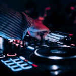 A person operates a DJ mixer and turntable with illuminated controls in a dimly lit environment at the Amsterdam Dance Event.
