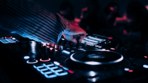 Everything You Need To Know Before Attending Amsterdam Dance Event A person operates a DJ mixer and turntable with illuminated controls in a dimly lit environment at the Amsterdam Dance Event.