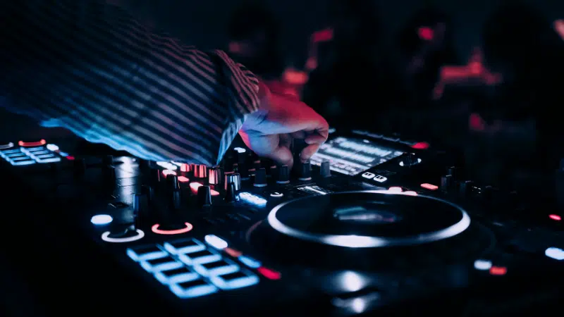 A person operates a DJ mixer and turntable with illuminated controls in a dimly lit environment at the Amsterdam Dance Event.
