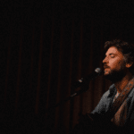 A man playing an acoustic guitar in a dark room, creating fresh new music.