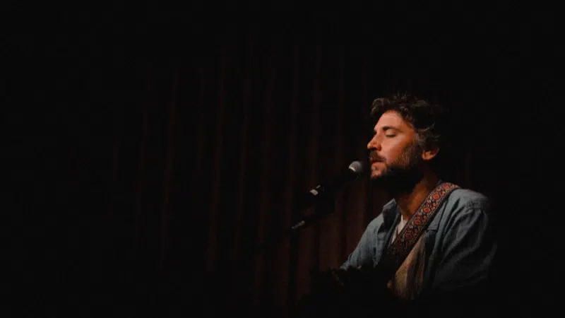 A man playing an acoustic guitar in a dark room, creating fresh new music.