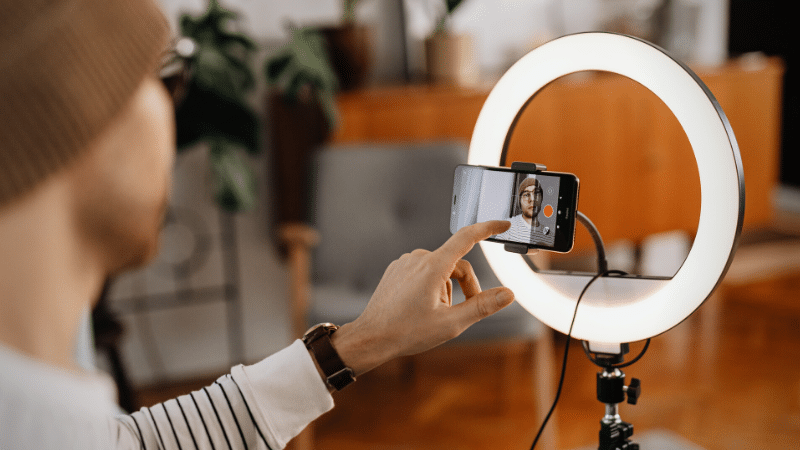 A man is taking a TikTok video with a ring light.
