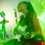 A woman playing a guitar in front of green smoke for her YouTube channel.