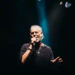 A man with a beard passionately singing into a microphone, delivering fresh new music.