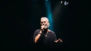 A man with a beard passionately singing into a microphone, delivering fresh new music.