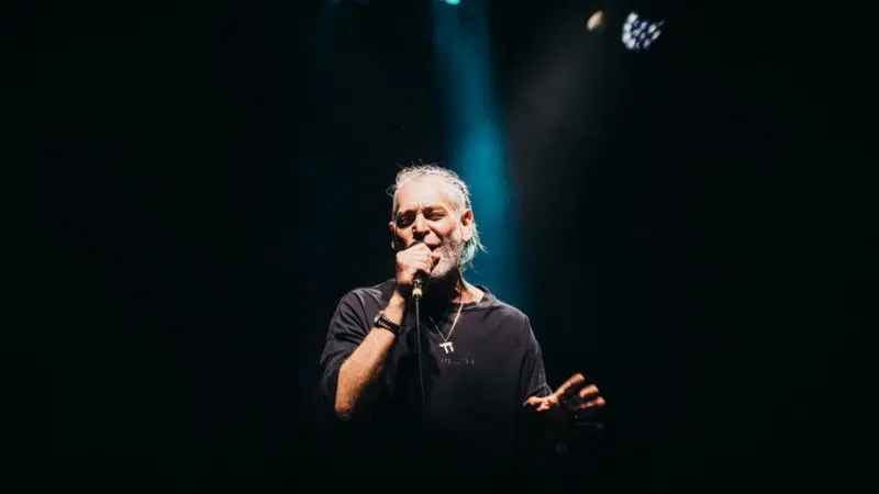 A man with a beard passionately singing into a microphone, delivering fresh new music.
