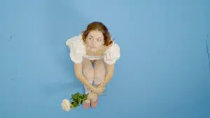 A fresh-faced girl is sitting on a vibrant blue background, delicately holding a beautiful flower.