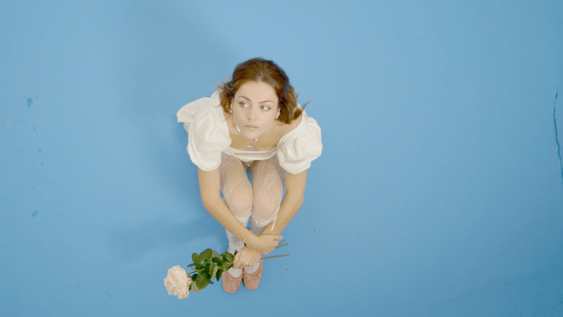 A fresh-faced girl is sitting on a vibrant blue background, delicately holding a beautiful flower.