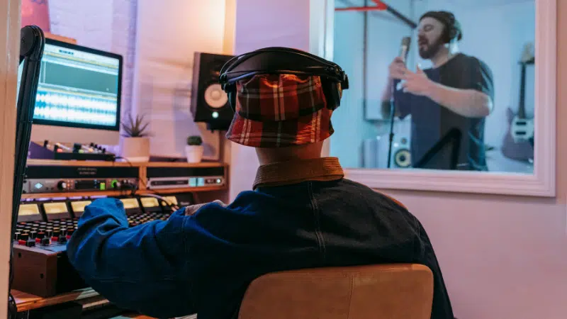 A man in a recording studio with a microphone in front of him, working on TIDAL collabs.