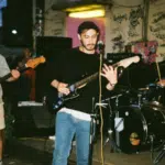 Under a starlit sky, a band performs outdoors, their music echoing against graffiti-covered walls. The guitarist sings passionately alongside the rhythmic beat of the drums and the bass's deep tones. This electrifying scene is perfect for marketing on Instagram, captivating an audience with its raw energy.