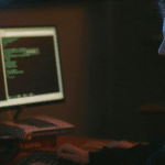 Woman focused on coding on a computer in a dimly lit room, with Spotify open in the background.