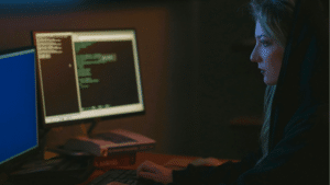 Woman focused on coding on a computer in a dimly lit room, with Spotify open in the background.