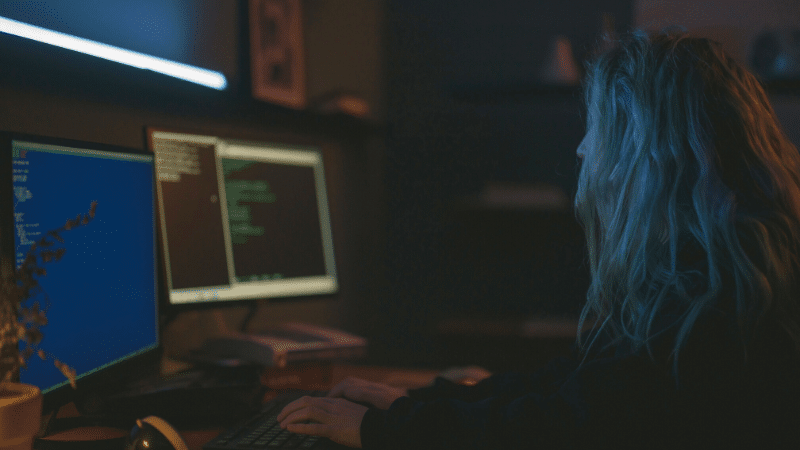 A woman browsing Spotify playlists while working at a computer in the dark.