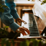 A person in a blue shirt plays a piano surrounded by lush green foliage indoors, creating a serene atmosphere reminiscent of the relaxing joy found during holidays.