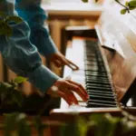 A person in a blue shirt plays a piano surrounded by lush green foliage indoors, creating a serene atmosphere reminiscent of the relaxing joy found during holidays.