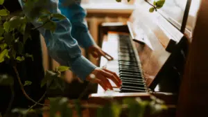 A person in a blue shirt plays a piano surrounded by lush green foliage indoors, creating a serene atmosphere reminiscent of the relaxing joy found during holidays.