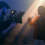 A man is filming another man in a room for a YouTube post-release.