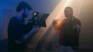 A man is filming another man in a room for a YouTube post-release.