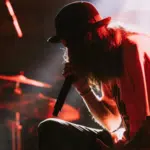 A man in a hat delivering exclusive content while singing on stage.
