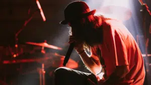 A man in a hat delivering exclusive content while singing on stage.
