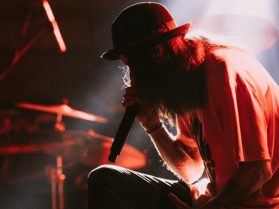 A man in a hat delivering exclusive content while singing on stage.