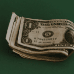 A small stack of folded one-dollar bills on a green background, subtly echoing the rhythm of how to make money with music.