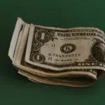 A small stack of folded one-dollar bills on a green background, subtly echoing the rhythm of how to make money with music.