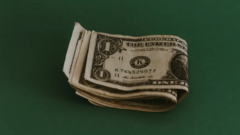 A small stack of folded one-dollar bills on a green background, subtly echoing the rhythm of how to make money with music.