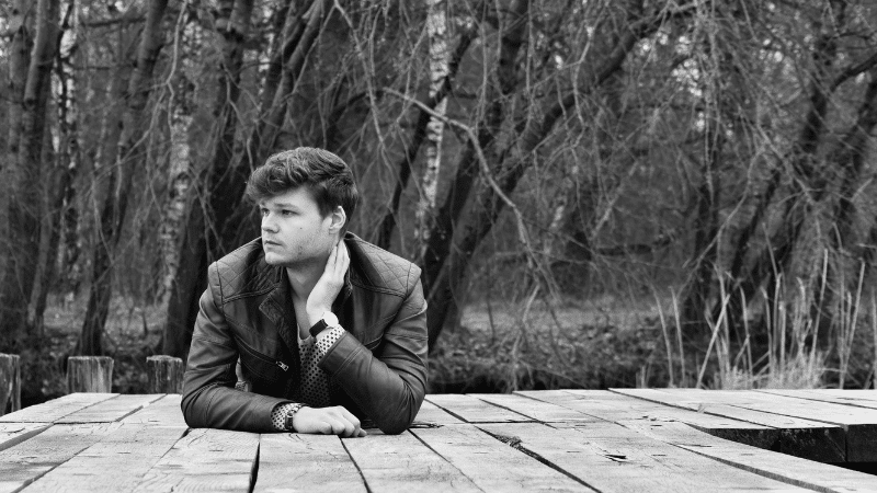 A man sitting on a dock in the woods, enjoying the peaceful ambiance while listening to fresh new music.