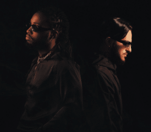 Two men with sunglasses standing in front of a black background.